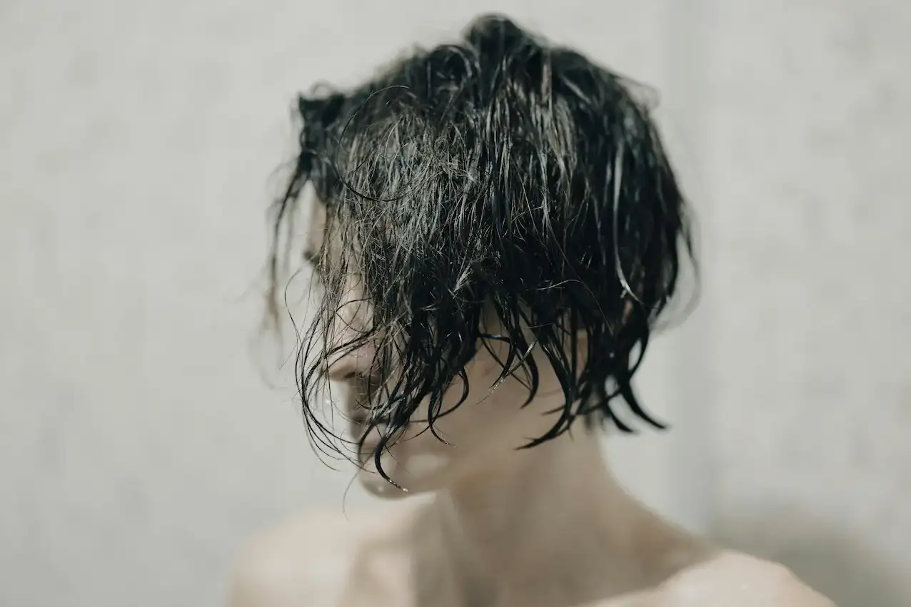 Woman with wet, dark hair falling across her face after washing, photographed against a neutral grey background.